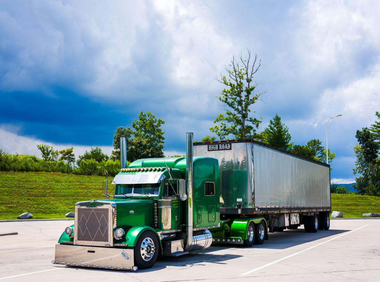 ours-journey A striking green semi-truck parked outdoors with a dramatic cloudy sky backdrop.